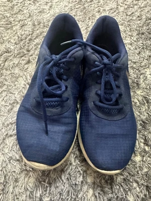 Marinblå sneakers - Snygga marinblå sneakers  med vit sula och klassisk vit swoosh på sidan. Skorna har lågt skaft, snörning och ovandel i textilmaterial som ger en sportig och clean look. Perfekta för dig som gillar stilrena och bekväma sneakers.