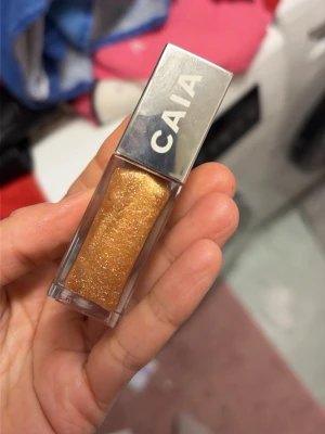 Guldig flytande ögonskugga från CAIA - Lipgloss från CAIA i en intensiv guldig nyans med massor av glitter. Kommer i en liten, rektangulär plastförpackning med silvrigt lock. Perfekt för dig som vill ha en .