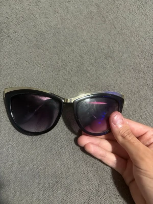 Glasögon - Snygga solglasögon i cat eye-modell med svart båge och guldfärgade detaljer upptill. Glasen är mörka och ger en cool look. Perfekta för dig som vill sticka ut och addera lite edge till din stil.