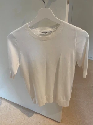 Vit stickad topp från Kappahl - En enkel och stilren vit stickad topp från Kappahl med rund halsringning och korta ärmar. Perfekt att matcha med jeans eller kjol för en clean look. Materialet känns mjukt och lätt mot huden. Endast testad