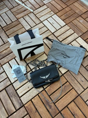 Zadigo voltaire väska - Köpt på NK i Göteborg för 3499kr, impulsköp och jag tycker att väskan är för liten. Väskan är så gott som ny. Allt på bilden ingår. På denna modellen av väska kan man ta av vingarna/loggan och byta ut. 
