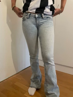 Ljusblå bootcut jeans - Säljer ett par ljusblå bootcut jeans med låg midja och klassisk femficksdesign. Jeansen har en snygg tvätt och är tillverkade i stretchigt denimtyg som sitter tajt över låren och släpper ut vid bensluten. Har lite slits där nere men är smutsiga tyvärr kan kanske gå bort i noggrann tvätt men vet ej 