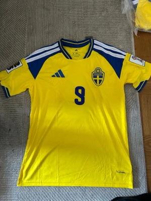 Svensk landslagströja Adidas gul/blå - Säljer en gul och blå svensk landslagströja från Adidas med nummer 9 på bröstet. Tröjan har korta ärmar, broderad landslagssköld och Adidas-logga. Tillverkad i lätt och ventilerande material, perfekt för fotboll eller träning.