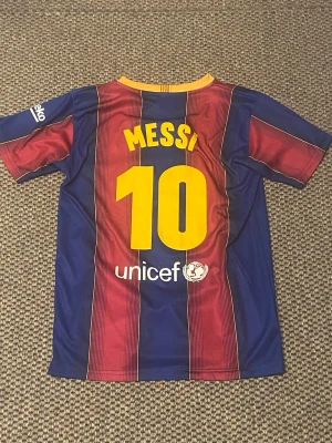 Barcelona Messi matchtröja blå/röd - Säljer en FC Barcelona matchtröja med Messi och nummer 10 på ryggen. Tröjan är blå och röd med gula detaljer, officiell klubbmärke på bröstet och Rakuten som sponsor. Tillverkad i lätt och ventilerande material, perfekt för fotboll eller träning.