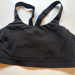Svart sport-bh med breda axelband strl.85c - Snygg svart sport-bh med breda, justerbara axelband och elastisk kant nedtill. Tillverkad i ett stretchigt material som ger bra stöd vid träning. Perfekt för gymmet eller löprundan. Från Kapp Ahl. Storlek 85c.