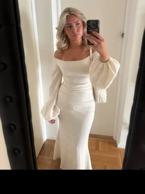 Adoore Reno dress - Elegant vit långklänning med offshoulder och långa puffärmar. Klänningen har en figurnära passform med lätt rynkade detaljer i midjan och är tillverkad i ett strukturerat tyg som ger en lyxig känsla. Perfekt för dig som vill sticka ut med en stilren look.  Använd vid ett tillfälle, säljes pga den inte passar längre. Verkligen superfin!!