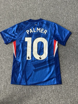 Chelsea FC matchtröja Palmer #10 - Snygg blå Chelsea FC matchtröja från Nike med Palmer och nummer 10 på ryggen. Tröjan har vita och röda detaljer på sidorna, klubbmärke och Nike-logga på bröstet. Tillverkad i lätt och ventilerande material, perfekt för fotboll eller träning.