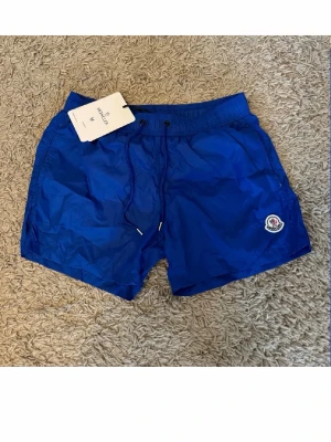 Blå badbyxor från Moncler - Snygga blå badbyxor från Moncler med elastisk midja och dragsko. Klassisk kort modell med Moncler-logga. Tillverkade i lätt och snabbtorkande material, perfekta för sommaren 