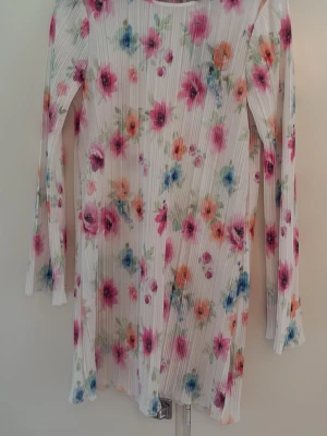 Vit blommig långärmad klänning HELT NY!  - Superfin vit klänning med färgglatt blommigt mönster i rosa, orange och blå toner. Klänningen har långärmad design och är gjord i ett lätt, plisserat material som ger en snygg struktur. Perfekt för vår och sommar! Helt ny! 