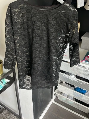 Svart spetsblus med trekvartsärm - Snygg svart blus i genombruten spets med trekvartsärm. Perfekt att styla lager på lager eller med ett linne under. Blusen har rund halsringning och är lätt transparent för en trendig look.