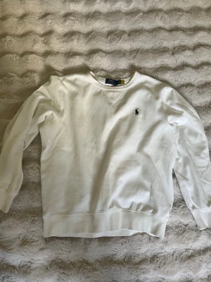 Vit stickad tröja från Polo Ralph Lauren - Snygg vit stickad tröja från Polo Ralph Lauren med klassisk rund hals och broderad marinblå logga på bröstet. Knappt använd har inga skadliga defekter.