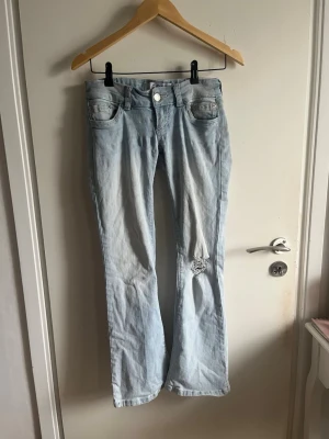 Ljusblåa lågmidjade jeans från G-rise - Midjemåttet ca 36cm Har inte bild på. Nypris ca 1400 Jeansen hade ett hål som lagats med påsydd lapp i samma färg. Säljer ett par ljusblå bootcut jeans från G-rise  med slitning och hål på ena benet. Jeansen har klassisk femficksdesign, låg midja och är tillverkade i denim. Perfekta för dig som gillar en avslappnad och trendig stil.