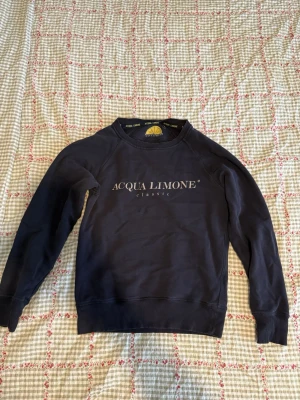 Mörkblå sweatshirt Acqua Limone - Mörkblå sweatshirt från Acqua Limone med klassisk logga framtill och stor gul citron-tryck på ryggen. Tröjan har rund hals, långa ärmar och ribbade muddar. 