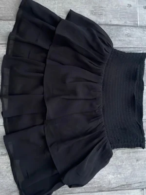 Svart volangkjol från KappAhl - Säljer en svart kortkjol från KappAhl med dubbla volanger och smock i midjan. Kjolen har en luftig och flowy känsla, perfekt för dig som gillar en feminin och trendig stil. Passar till många olika looks och är superenkel att matcha.