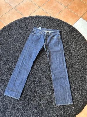Blå raka jeans från Levi's - Klassiska blå jeans från Levi's med rak passform och fem fickor. Jeansen har synliga sömmar och en läderpatch bak i midjan. Tillverkade i slitstark denim med en tidlös look som funkar till det mesta.