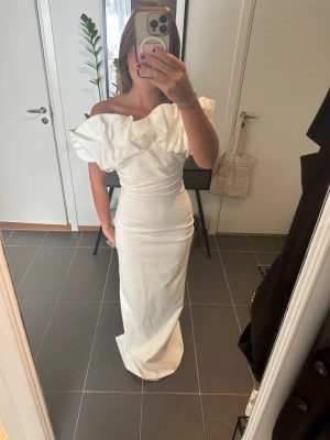 Balklänning - Elegant vit långklänning med offshoulder och stor volang upptill. Klänningen har figurnära passform och är perfekt för speciella tillfällen t.ex bal. Köpt för 3500kr, den är aldrig använd endast provad🤍 Säljer pga att jag köpt en ny! 