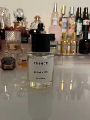 ESSNCE Sugar Kiss Eau de Parfum - ESSNCE Sugar Kiss Eau de Parfum i en stilren, rund glasflaska med svart lock. Parfymen har en ljusgul vätska och minimalistisk etikett. Perfekt för dig som gillar söta och fräscha dofter med modern känsla.