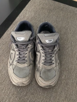 Gråa skor - Snygga grå sneakers med chunky sula och coola paneler i mesh och läder. Skorna har gråa skosnören och detaljerad design med logga på plösen och hälen. Perfekta för dig som gillar streetwear och exklusiva märken.