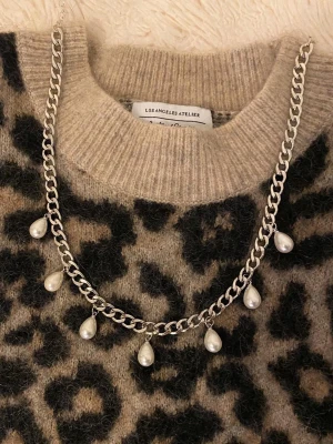 Silverfärgat halsband med pärldroppar - Stilrent halsband i silverfärgad metall med sju droppformade pärlor som hänger längs kedjan. Perfekt accessoar för att lyfta din outfit med en trendig och elegant touch.