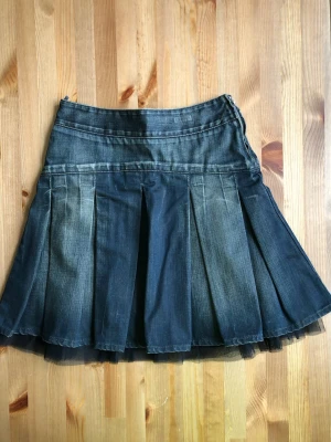 Mörkblå plisserad jeanskjol - Snygg mörkblå jeanskjol med plisserad design och dragkedja i sidan. Kjolen har en klassisk denimlook och är perfekt för dig som gillar en avslappnad men trendig stil.