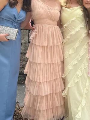 Gammel rosa balklänning med volang - Snygg gammel/baby rosa balklänning med oneshoulder-design och volangdetaljer i flera lager. Klänningen har markerad midja och dragkedja i sidan för enkel påklädning. Perfekt till balen eller andra fina tillfällen, sitter bra på mig som har S. Även använd en gång och köpt här ifrån plick