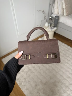 Brun handväska från Glitter - Snygg brun handväska i mockaimitation. Väskan är från göitter och är använd max två gånger, super fin och är i ett mycket bra skick.