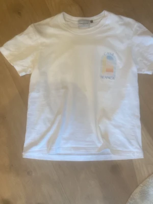 Vit t-shirt från Casablanca - Vit t-shirt från Casablanca med färgglatt tryck och texten 'Casa Blanca' både fram och bak. Klassisk passform och rund halsringning. Tillverkad i mjuk bomull, perfekt för en chill och stilren look.