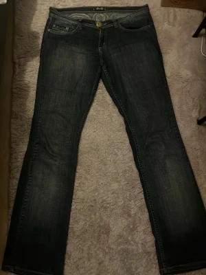 Lågmidjade D&G jeans  - Snygga lågmidjande jeans från Dolce & Gabbana med en stor D&G-logga i grått på baksidan. Midjemått: 41cm Inrebenmått: 77cm vilket motsvarar ca W32 L30. 