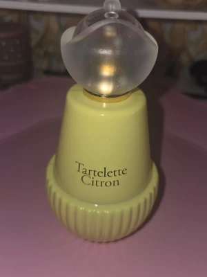 Tartelette Citron parfym - Fräsch parfym med toppnoter av citron, ingefära och äpple. Mellannoter av jasmin, fresia och vita träslag samt basnoter av mysk, ceder och amber. Flaskan är ljusgul med en rund, frostad kork och har en söt, lekfull design.