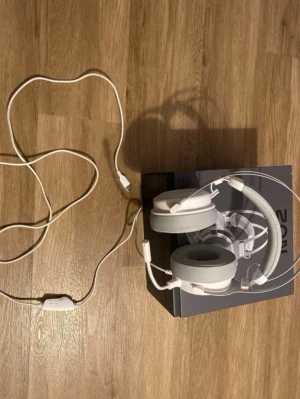 ZON gaming headset i vitt - Säljer ett ZON gaming headset i vit färg med stora, rundade öronkuddar och justerbar huvudbygel. Headsetet har inbyggd mikrofon och lång vit kabel med kontroll. Materialet är en kombination av plast och mjukt konstläder för komfort under långa gaming-sessioner.