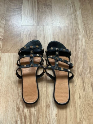 Svarta sandaler med nitar - Snygga svarta sandaler med flera remmar dekorerade med guldiga pyramidnitar. Storlek 36,5