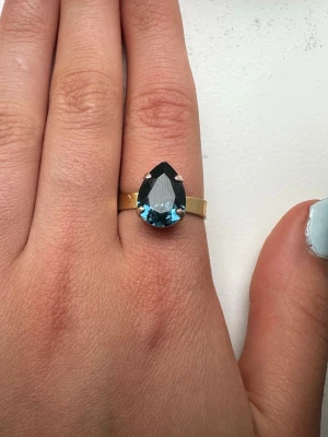 Guldring med blå sten Caroline svedblom - Snygg guldfärgad ring med en stor, droppformad blå sten som mittpunkt. Lite färg har kommit av men syns knappt