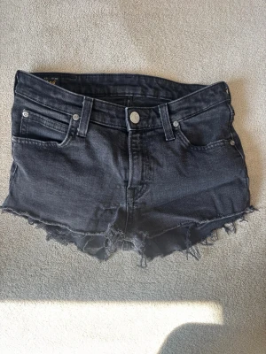Svarta jeansshorts Lee - Säljer ett par svarta jeansshorts från Lee med råa, fransiga kanter och klassisk femficksdesign. Shortsen har knappgylf och bälteshällor, perfekt för en avslappnad look. Materialet är slitstark bomull med en mörk tvätt.