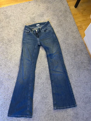 Blå bootcut jeans med broderade fickor - Snygga blå bootcut jeans med klassisk femficksdesign och broderade detaljer på bakfickorna. Jeansen har låg midja och är tillverkade i denim med lätt stretch för skön passform. Perfekta för en avslappnad och trendig look.