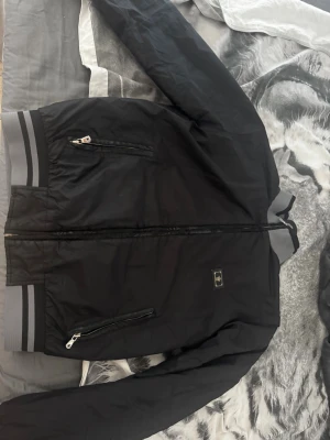 Äkta Dolce & Gabbana Jacka - Snygg svart bomberjacka från Dolce & Gabbana. Nypris 15 000kr. Jackan har två fickor med dragkedja och ett diskret DG-emblem på bröstet. Materialet är lätt och jackan har klassisk bomberform. Perfekt för dig som vill ha en stilren look. Säljs för 999, men priset kan diskuteras