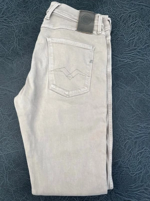 Ljusgrå jeans från Replay - Snygga ljusgrå jeans från Replay med klassisk femficksdesign och diskreta sömmar på bakfickan. Jeansen har normal midja, raka ben och är tillverkade i mjuk denim med stretch för extra komfort. Perfekta för en stilren och avslappnad look. Storlek W33 L34