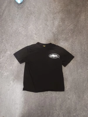 Corteiz T-shirt - Svart t-shirt med rund hals och korta ärmar. På bröstet och ryggen finns ett vitt tryck med ett ovalt motiv. Perfekt för en avslappnad och stilren look.