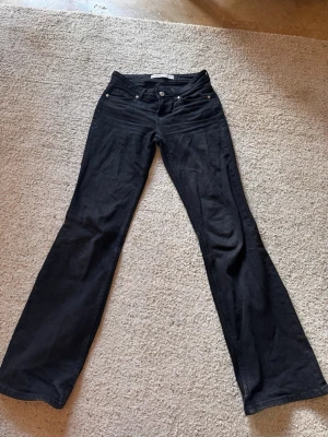 Svarta bootcut jeans med låg midja - Snygga svarta bootcut jeans med låg midja. Jeansen har utsvängda ben och är tillverkade i ett stretchigt bomullsmaterial. Perfekta för dig som gillar en retroinspirerad look.