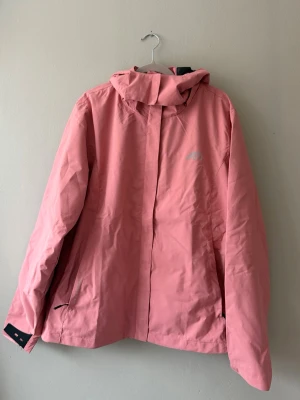 Rosa vindjacka - Snygg rosa vindjacka med huva och dragkedja framtill. Jackan har justerbara ärmslut med kardborre och två fickor med dragkedja. 