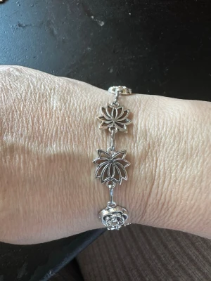 Silverfärgat armband med blommor - Snyggt armband i silverfärgad metall med detaljerade blomformade länkar. Armbandet har både lotusliknande och runda blommotiv som ger en cool och bohemisk vibe. Perfekt accessoar för att lyfta din stil med en unik touch.