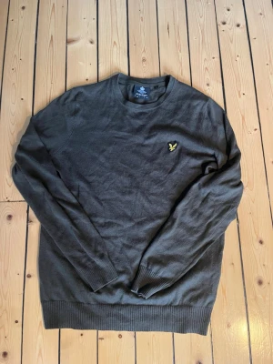 Lyle & Scott tröja - Mörkgrå långärmad tröja från Lyle & Scott med rund halsringning och klassisk gul logga på bröstet. Tröjan har ribbade muddar vid ärmslut och nederkant. Perfekt för en stilren och enkel look.
