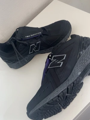 Svarta New Balance sneakers - Snygga svarta sneakers från New Balance med stora silvriga N-loggor på sidorna. Skorna har en chunky sula, meshdetaljer och reflekterande partier. Klassisk snörning och sportig look som passar till streetwear.