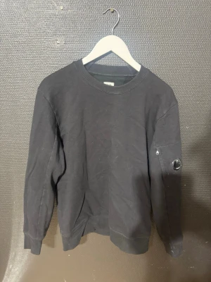 C.P. Company sweatshirt - Svart sweatshirt från C.P. Company. Tröjan har en klassisk passform och en ikonisk linsdetalj på ena ärmen. Perfekt för en avslappnad och stilren look. Storlek M 