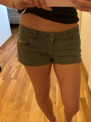 Lågmidjade Olivgröna shorts från H&M - Snygga olivgröna lågmidjade shorts från H&M med klassisk femficksdesign och uppvikta benslut. De har normal passform och stängs med knapp och dragkedja. Perfekta för varma dagar och enkla att matcha med olika toppar. Köpte på Vinted förra året, använda fåtal gånger. Inga defekter. Midjemåttet är 36💕💕💕 säljer då de är förstora för mig 