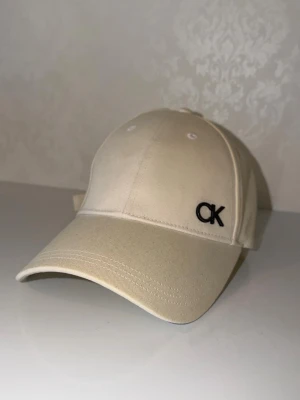  keps från Calvin Klein - Snygg  keps från Calvin Klein med broderad svart CK-logga framtill. Klassisk böjd skärm och justerbar rem bak.  Perfekt accessoar för en clean och stilren look.