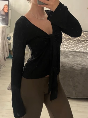 Svart topp med knytning - Säljer denna superfina topp med knytning från GinaTricot! Superfin passform med öppet tyg över magen, med knytning emellan som man kan knyta hur man vill och utsvängd vid armarna. Har endast använt den ett fåtal gånger och därför är skicket jättebra fortfarande!
