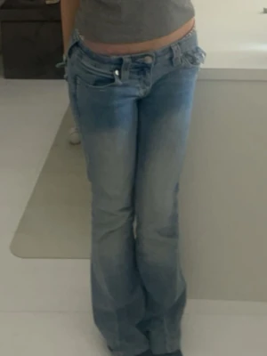Ljusblå bootcut jeans - Säljer ett par ljusblå bootcut jeans med låg midja och klassiska fem fickor. Jeansen har slitningar och en avslappnad passform, perfekta för en casual look. Inget synligt märke men riktigt snygga till vardagsstilen.