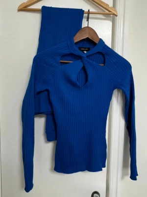 Blått ribbat set med cut out-detalj - Säljer ett blått ribbat set från New Look med långärmad topp och matchande byxor. Toppen har en snygg cut out-detalj framtill och åtsittande passform. Materialet är stretchigt och mjukt, perfekt för dig som gillar trendiga och bekväma plagg. Använd en gång.