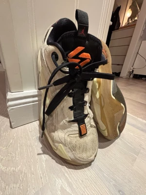 Jordan sneakers beige och svart - Säljer ett par feta Jordan sneakers i beige med svarta detaljer och orange logga på plösen. Skorna har en chunky sula, mesh och syntetmaterial på ovandelen samt klassisk Jumpman-logga på sidan. Perfekta för dig som gillar streetwear och vill sticka ut.
