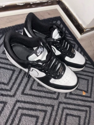 Nike svartvita sneakers - Snygga svartvita Nike sneakers med klassisk design. Skorna har svart ovandel med vita detaljer och vit sula. Perforerad tå för extra ventilation och bekvämt foder. Perfekta för dig som gillar streetstyle och sportig look.